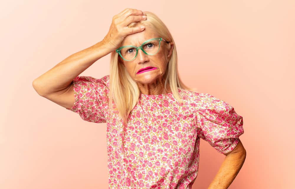 middle age womanmaking midlife weird face with hand on forehead wearing glasses
