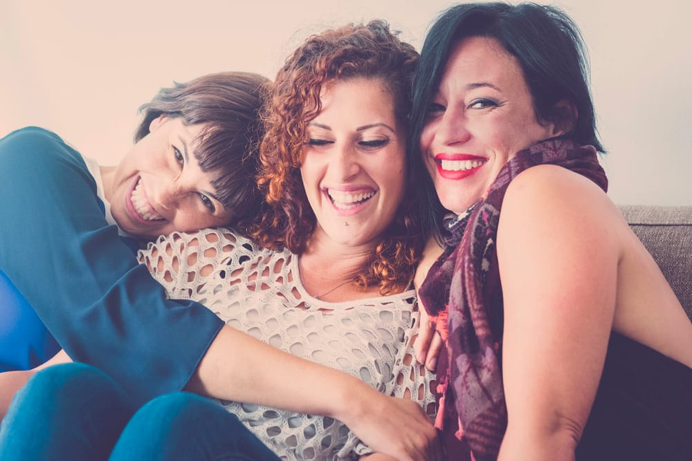 cheerful females middle age young womane friends together sitting on a sofa at home in leisure activity indoor. smile and enjoy the day hugging and touching with care and friendship